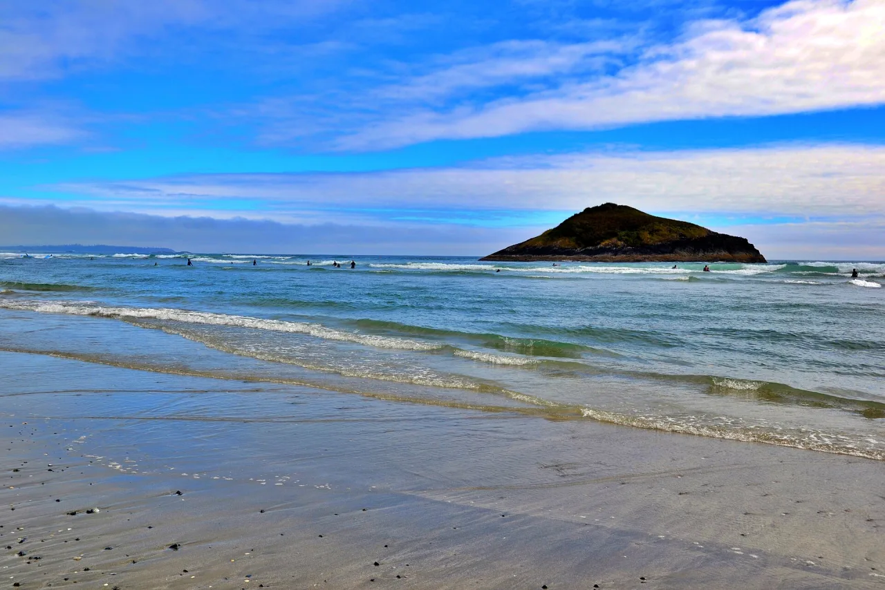 Lone Rock standing off wide, wet sand at Long Beach under a blue sky