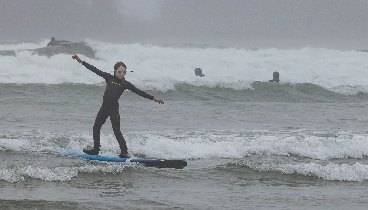 A surfer riding a small wave in front of misty forested headlands near Tofino